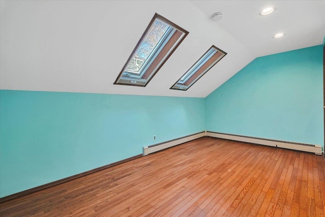 additional living space with a baseboard radiator, vaulted ceiling with skylight, and light wood-style flooring