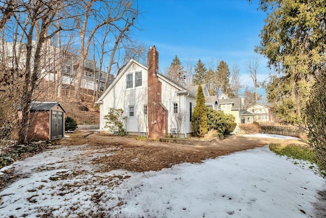 snow covered property with an outbuilding, a storage unit, a chimney, and a residential view