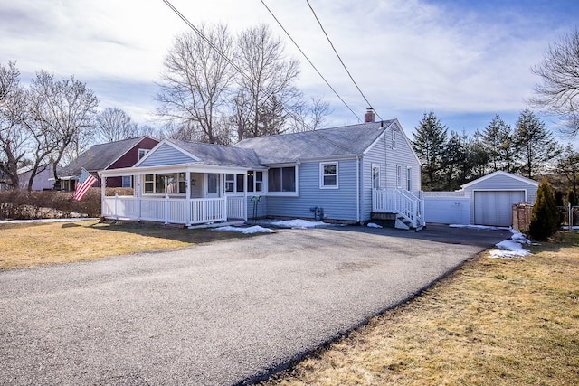 ranch-style home with aphalt driveway, a detached garage, a chimney, a porch, and an outdoor structure