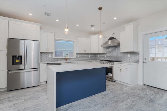 kitchen featuring white cabinetry, hanging light fixtures, a center island, appliances with stainless steel finishes, and wall chimney range hood