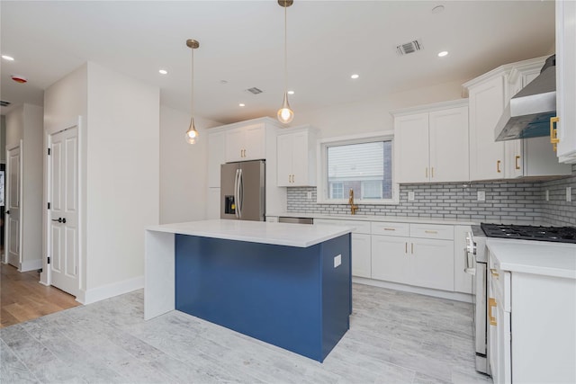 kitchen with white cabinetry, a kitchen island, appliances with stainless steel finishes, wall chimney exhaust hood, and pendant lighting