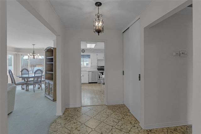 corridor featuring a chandelier, light floors, and baseboards