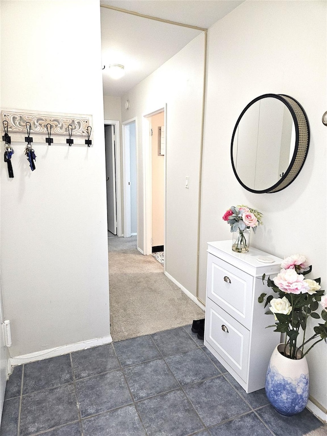 hall featuring baseboards and dark colored carpet