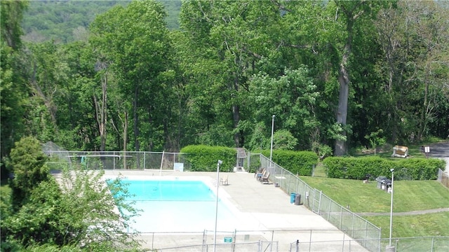 view of swimming pool featuring a patio, fence, a wooded view, a fenced in pool, and a lawn