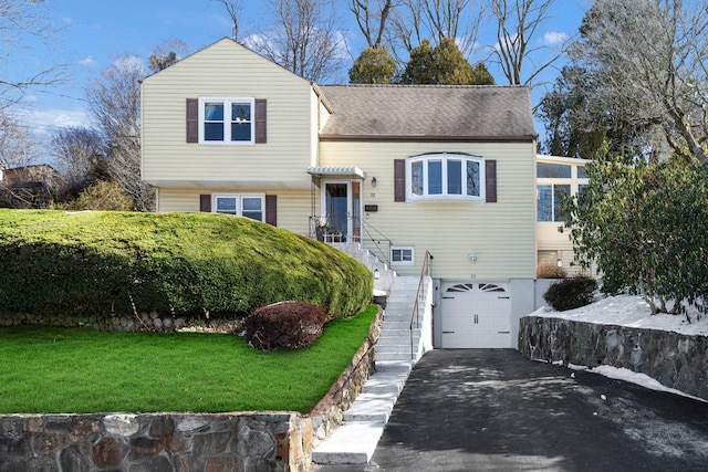 tri-level home with aphalt driveway, a garage, a shingled roof, stairway, and a front yard