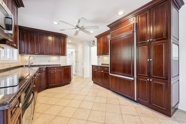 kitchen featuring light tile patterned floors, tasteful backsplash, stainless steel microwave, a ceiling fan, and a sink