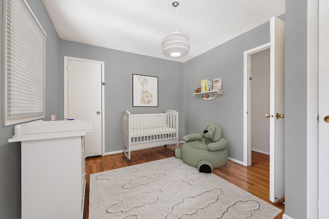 bedroom featuring a nursery area, baseboards, and wood finished floors