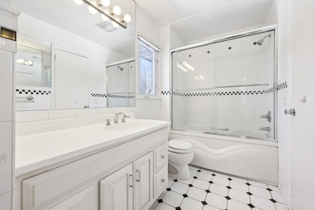 full bath with tile walls, toilet, combined bath / shower with glass door, vanity, and tile patterned floors