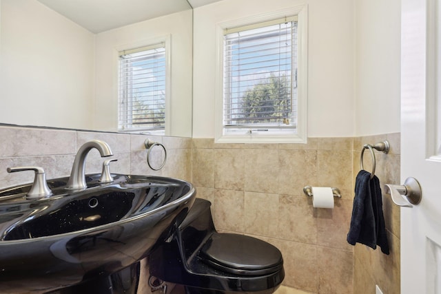 half bathroom featuring wainscoting, a sink, tile walls, and toilet