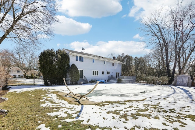 snow covered rear of property with a storage shed, a chimney, and an outdoor structure