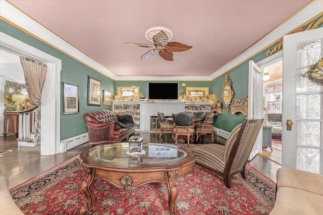 living room featuring wood-type flooring, ceiling fan, ornamental molding, a brick fireplace, and a baseboard heating unit