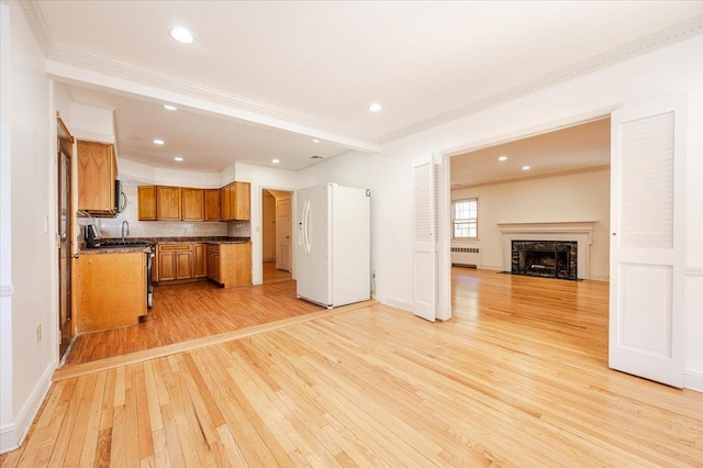 kitchen with white refrigerator with ice dispenser, brown cabinets, dark countertops, radiator, and open floor plan