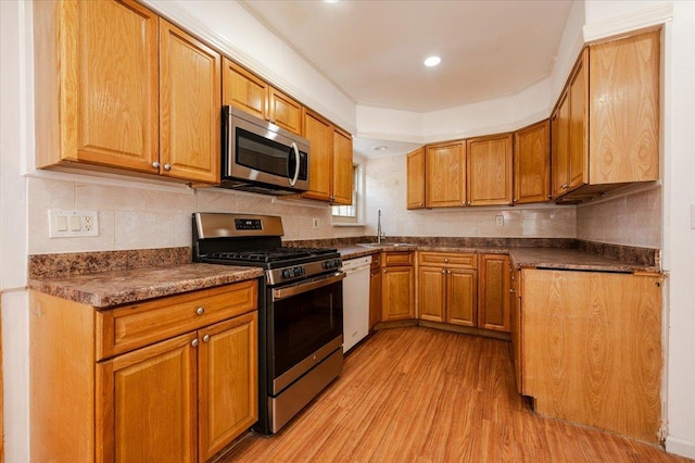 kitchen with dark countertops, light wood-style flooring, brown cabinets, stainless steel appliances, and a sink