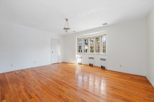 unfurnished room featuring radiator, light wood finished floors, and visible vents