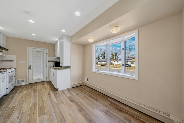 kitchen with a baseboard radiator, white cabinetry, backsplash, light wood finished floors, and gas range gas stove