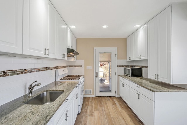 kitchen with under cabinet range hood, white gas range, a sink, and white cabinets