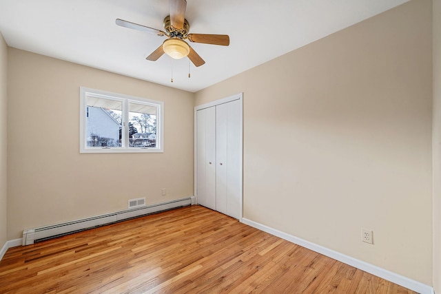 unfurnished bedroom featuring baseboards, ceiling fan, a baseboard radiator, light wood-style flooring, and a closet