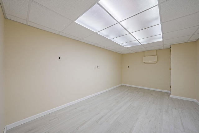 finished basement featuring a paneled ceiling, light wood-style floors, baseboards, and a wall mounted AC