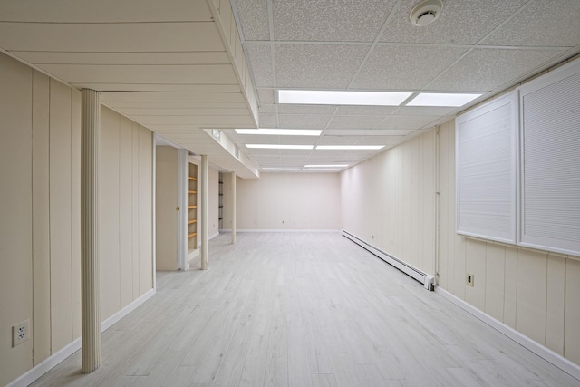 finished basement with a baseboard heating unit, a drop ceiling, and light wood-style flooring