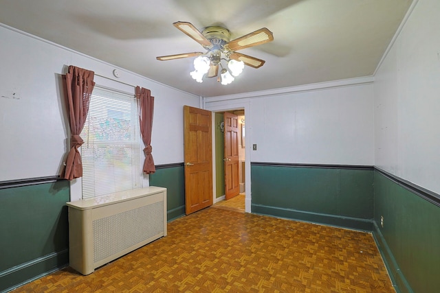 unfurnished room with radiator heating unit, ceiling fan, and crown molding