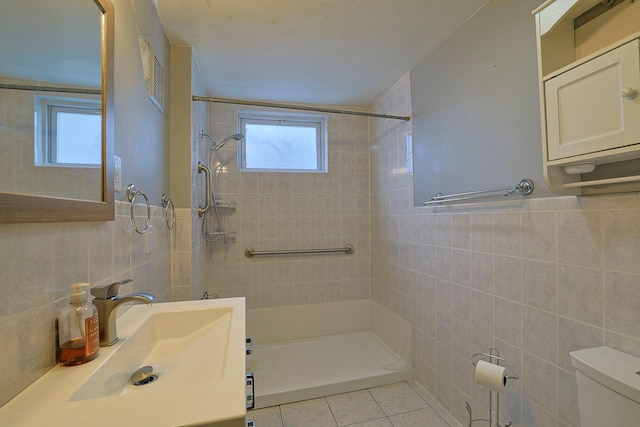 bathroom with tile patterned flooring, toilet, tile walls, tiled shower, and wainscoting