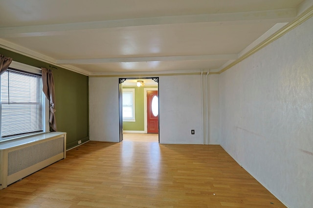 spare room featuring radiator, light wood-style floors, and beamed ceiling