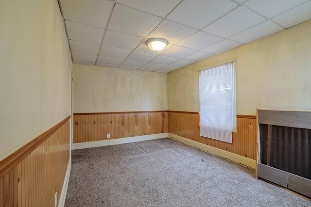 carpeted spare room with a wainscoted wall, wooden walls, and a drop ceiling