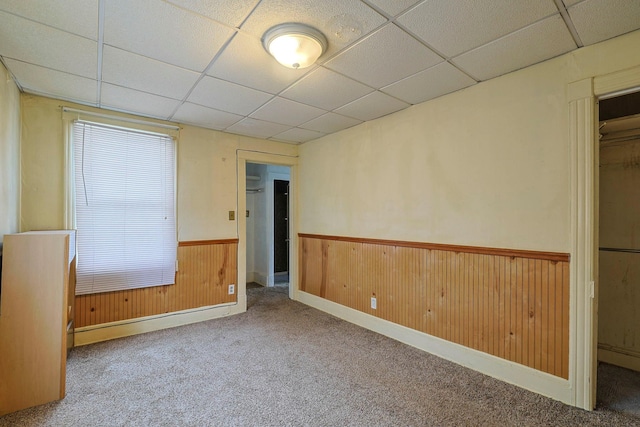 carpeted spare room with a paneled ceiling, a wainscoted wall, wooden walls, and baseboard heating