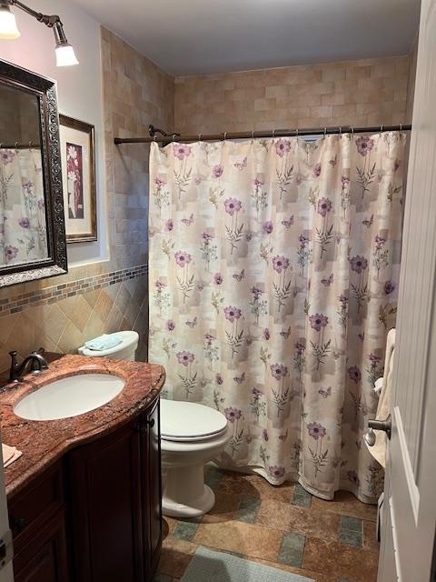 bathroom featuring toilet, tile walls, vanity, and walk in shower