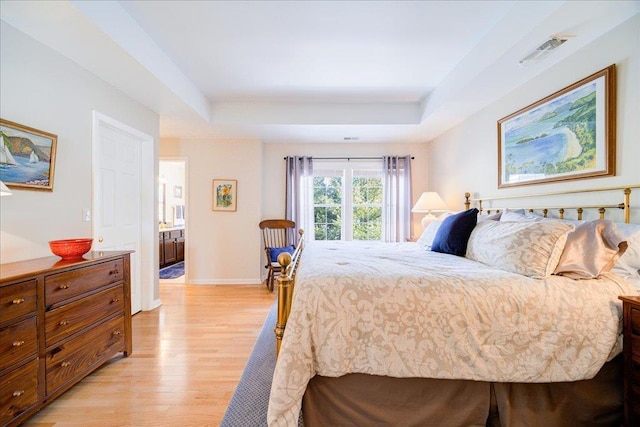 bedroom with light wood-type flooring and a tray ceiling