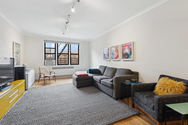 living area with radiator, ornamental molding, track lighting, wood finished floors, and cooling unit