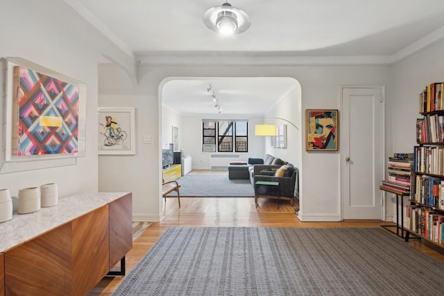 hallway with baseboards, ornamental molding, arched walkways, and light wood-style floors