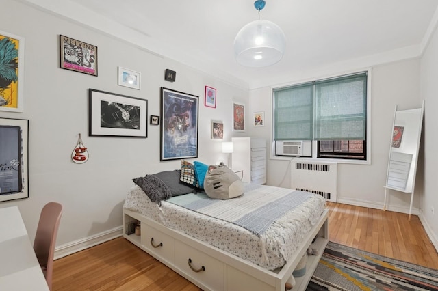 bedroom featuring baseboards, cooling unit, light wood-style flooring, and radiator