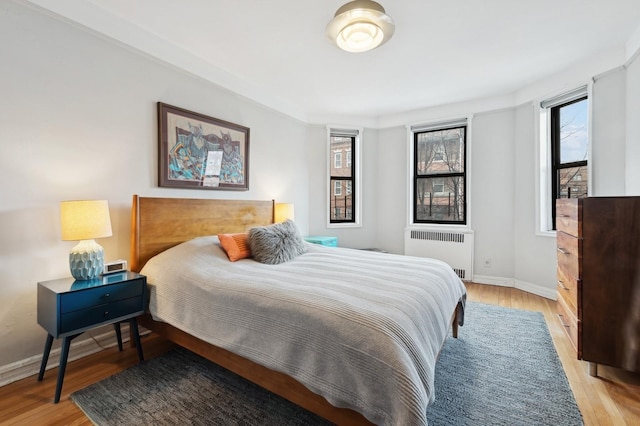 bedroom with baseboards, light wood-style flooring, and radiator heating unit