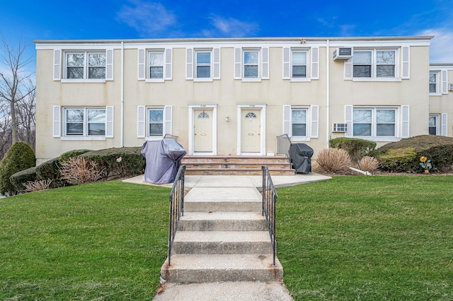 view of front facade featuring entry steps, a wall mounted air conditioner, a front yard, and stucco siding