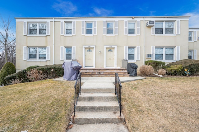 multi unit property with entry steps, a wall mounted air conditioner, a front lawn, and stucco siding