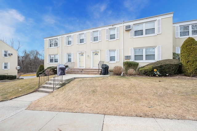 multi unit property featuring a wall mounted AC, a front lawn, and stucco siding