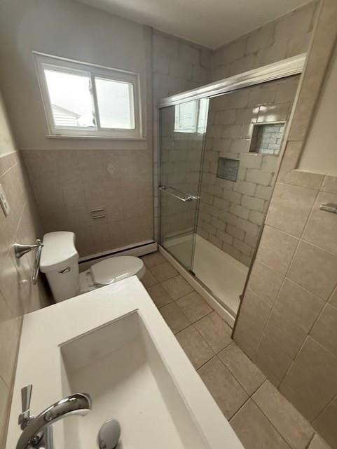 bathroom with a shower with door, tile patterned floors, a baseboard heating unit, toilet, and tile walls