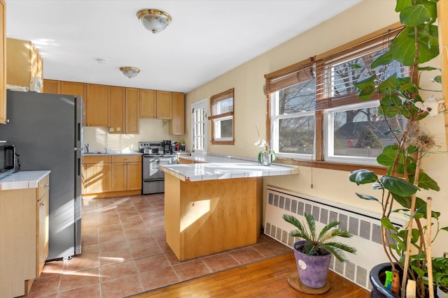 kitchen featuring tile countertops, radiator heating unit, a peninsula, stainless steel appliances, and a sink