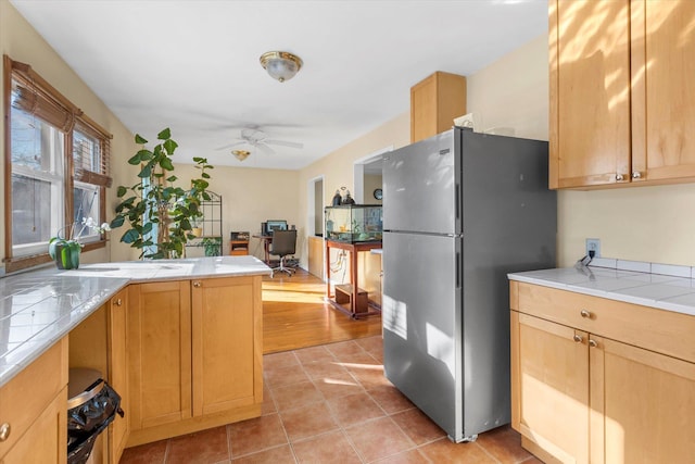 kitchen featuring light tile patterned floors, a ceiling fan, tile countertops, freestanding refrigerator, and a peninsula