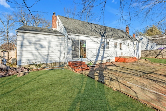 rear view of property featuring entry steps, fence, roof with shingles, a lawn, and a chimney