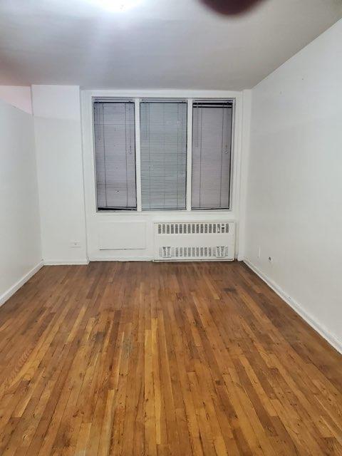 unfurnished room with radiator, baseboards, and wood finished floors