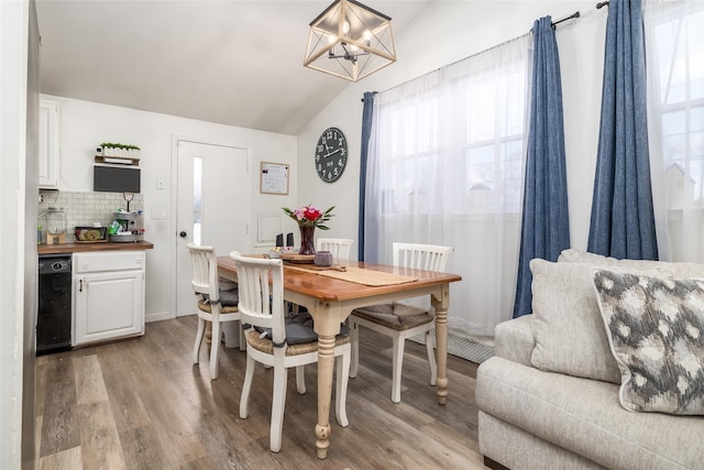 dining space with an inviting chandelier, light wood-type flooring, and vaulted ceiling