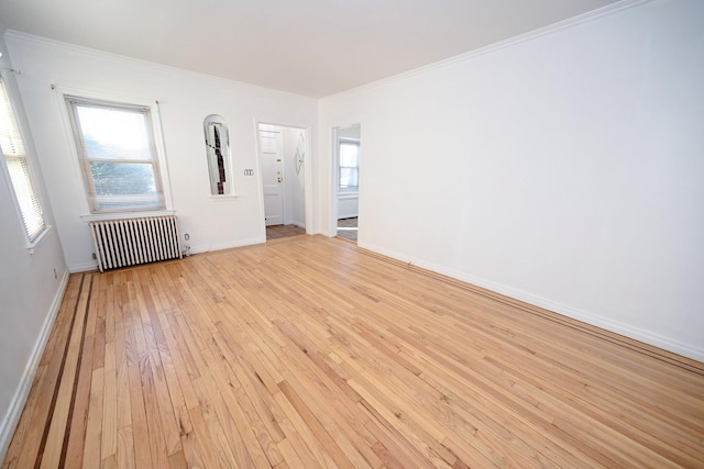 spare room with ornamental molding, radiator, baseboards, and light wood finished floors