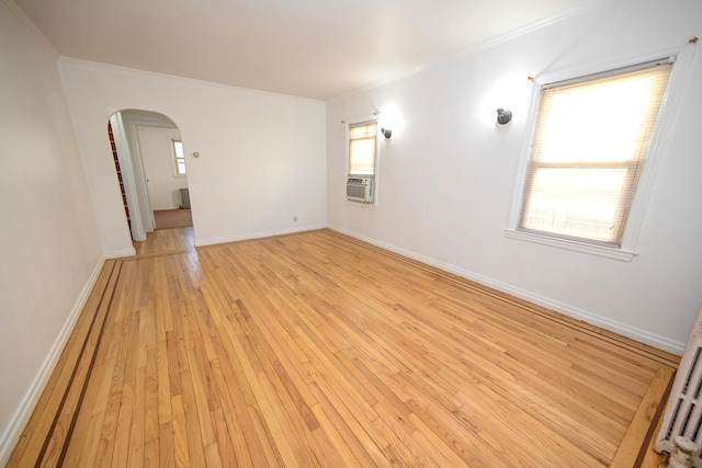 empty room featuring light wood-style floors, arched walkways, ornamental molding, and baseboards