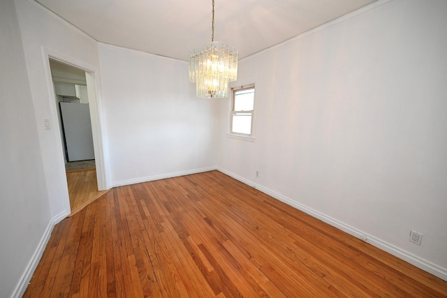 empty room featuring a notable chandelier, wood finished floors, and baseboards