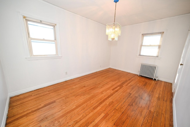 spare room featuring radiator, light wood finished floors, baseboards, and a chandelier