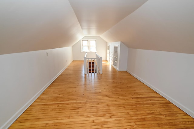 additional living space with light wood-style floors, built in shelves, baseboards, and vaulted ceiling