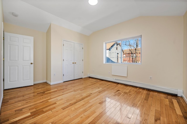 unfurnished bedroom with baseboard heating, light wood-type flooring, a closet, and lofted ceiling