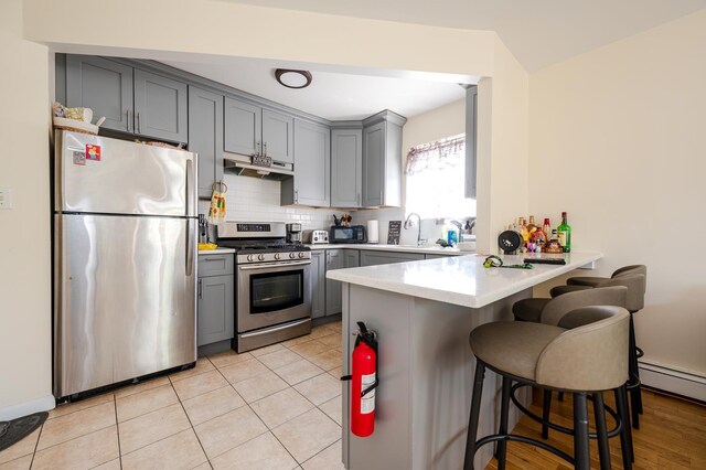 kitchen featuring kitchen peninsula, gray cabinets, tasteful backsplash, appliances with stainless steel finishes, and a breakfast bar area